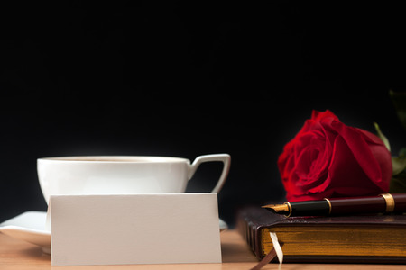Red rose, cup of coffee, sheet of paper and fountain pen on the tableの写真素材