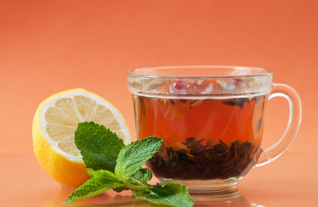 Cup of tea, lemon and mint leaves on a orange background