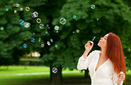 Beautiful young red-haired woman and bubbles on outdoorsの写真素材