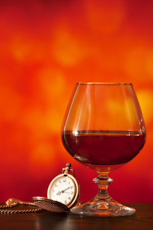 Brandy glass and pocket watch on the bright blurred background with bokehの写真素材
