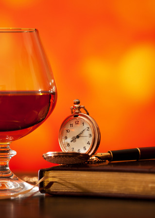 Brandy glass, diary and pocket watch on the bright blurred background with bokehの写真素材
