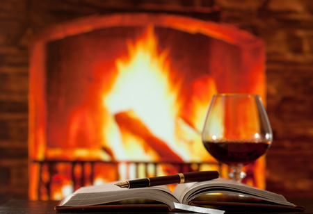 Diary and brandy glass on the table near the burning fireplaceの写真素材