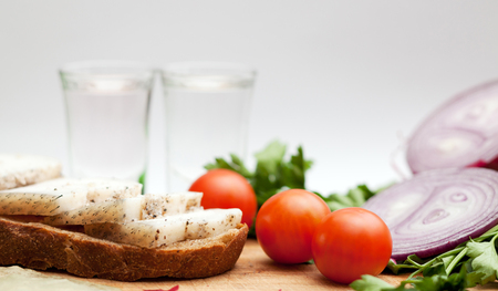 Lard on bread, tomatoes, onions, fresh herbs and vodka on a white backgroundの写真素材
