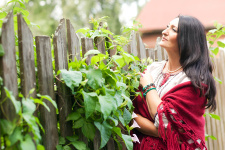 Beautiful adult village woman in a shawl near a wooden fenceの写真素材