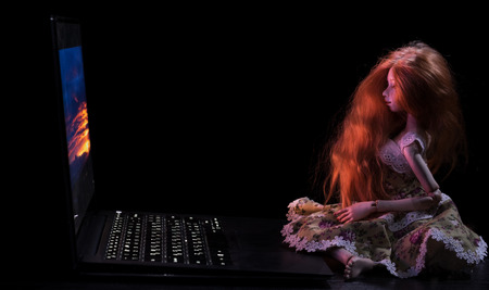 Beautiful red-haired doll and laptop on a black backgroundの写真素材