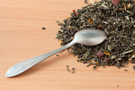 Background with green tea. Dried green tea leaves on the table. Spilled tea leaves and a teaspoon.の写真素材