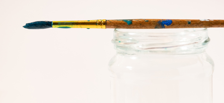 Paint brush in the paint lies on a jar of water on a white background