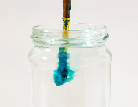 Brush with paint in a jar of water on a white backgroundの写真素材