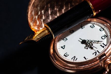 Golden beautiful pocket watch and fountain pen close up on black
