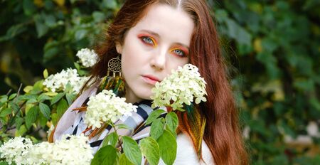 beautiful woman with red hair and bright makeup near flowers on the nature