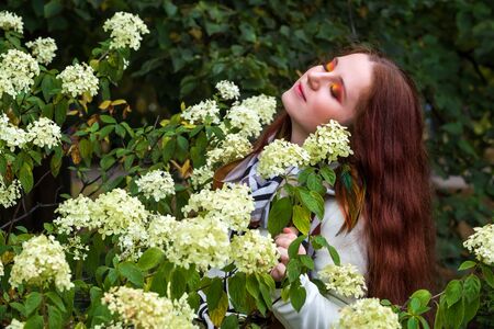 beautiful woman with red hair and bright makeup near flowers on the natureの写真素材