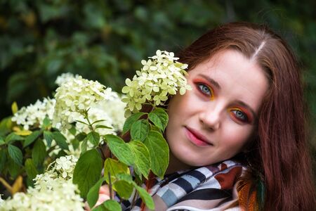 beautiful woman with red hair and bright makeup near flowers on the natureの写真素材