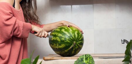 woman in the kitchen cuts a green watermelonの写真素材