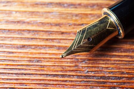 closeup of a golden fountain pen on a embossed wooden tableの写真素材