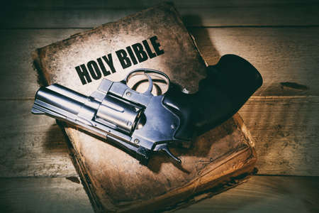 chrome revolver on an old bible on a wooden table