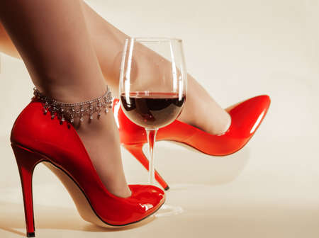 female feet with chain decoration in patent leather shiny red stiletto heels and wine glassの写真素材