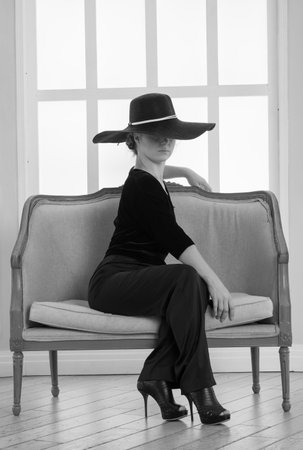 beautiful woman in a big hat sits on the background of the windowの写真素材