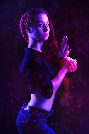 beautiful woman with long red hair and revolver in hands on violetの写真素材