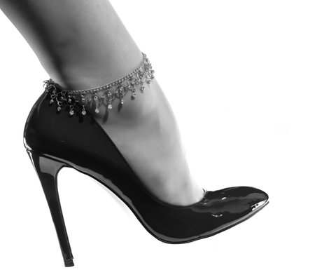 beautiful female leg with a decorative chain in a shiny black patent leather shoe on a whie
