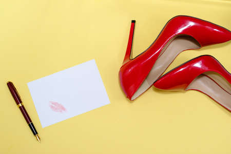 beautiful female shiny red stilettos and a card with a lipstick print on a yellow backgroundの写真素材