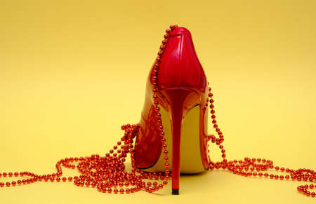 beautiful patent leather shiny female red stilettos and beads on a yellow backgroundの写真素材