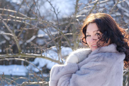 portrait of a beautiful adult woman in a fur coat and mittens outdoors in winterの写真素材
