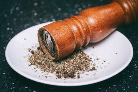 ground black pepper in a white saucer and a wooden millの写真素材