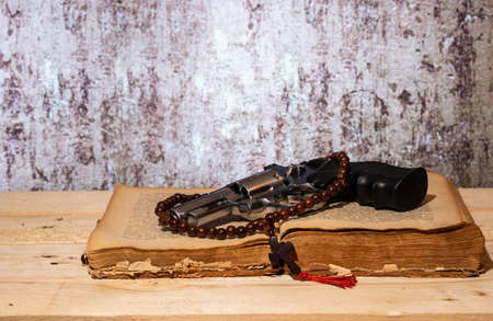 chrome revolver and cross on an old book on a wooden tableの写真素材