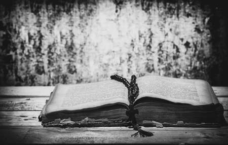 an old open book and cross lies on a wooden tableの写真素材