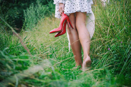 a woman walks barefoot on the grass in summer holding shoes in her handsの写真素材