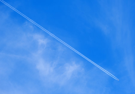 a flying plane against a blue sky and a long white trail behind itの写真素材