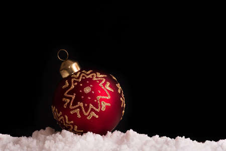 beautiful Christmas red ball with gold ornament in the snow on a black backgroundの写真素材