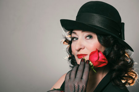 beautiful stylish woman in a hat and gloves holds a red rose in her hands near her lips