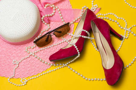 beautiful pink summer women's hat, red shoes, sunglasses and pearl beads lie on a yellow background