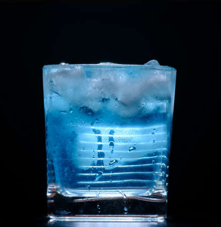 glass with ice and blue cocktail on black backgroundの写真素材