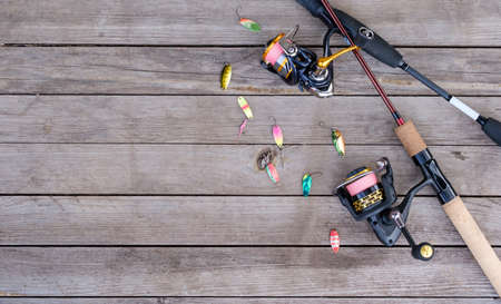 two spinning rods with reels and fishing lures lie on a wooden table top viewの写真素材