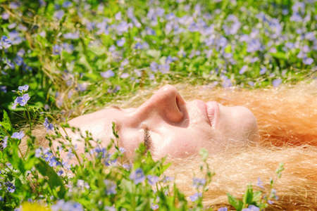face of a woman with red hair in the grass among small beautiful purple flowersの写真素材