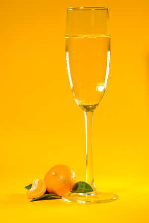 beautiful small ripe tangerine with green leaves and a glass of champagne on a yellow backgroundの写真素材