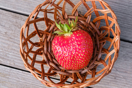 beautiful big ripe red strawberry lies in a small basket on a wooden tableの写真素材