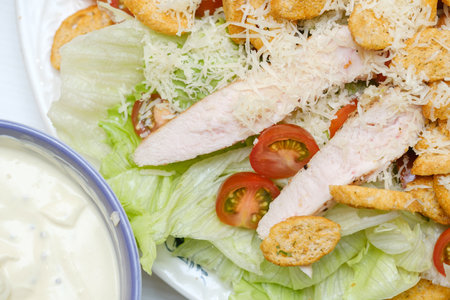 fresh Caesar salad with chicken and croutons close-up in a plate next to the sauceの写真素材