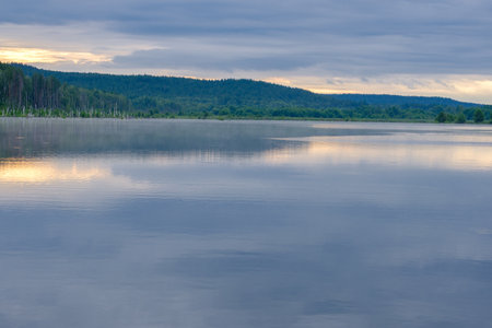 wide river and forest on the horizon on an early summer cloudy morning