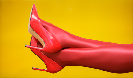 female legs in red shiny leather stiletto heels and red tights on yellow background