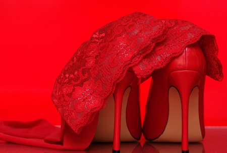 red shiny patent leather stiletto heels and red stockings on a red background