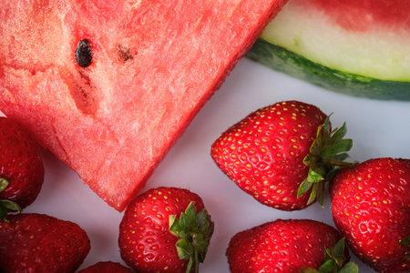 sliced watermelon wedges and red strawberries lie on a white plate close-up