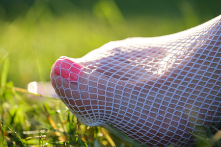Women's toes with a red pedicure and white fishnet stockings on green grassの写真素材