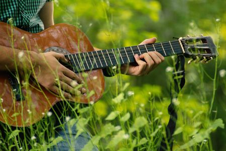 Play guitar in nature. Sitting with guitar in grass. Populat music instrument.の写真素材
