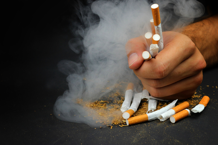 Destroyed cigarettes in hand with smoke. Symbol for Stop smoking.の写真素材