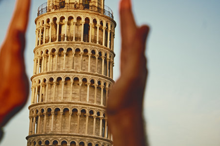 Leaning Tower of Pisa framed by blurred hands from sides, warm evening sunlight, golden tones, partial view, Italian landmark, travel inspiration, soft focus, right space for text.の写真素材