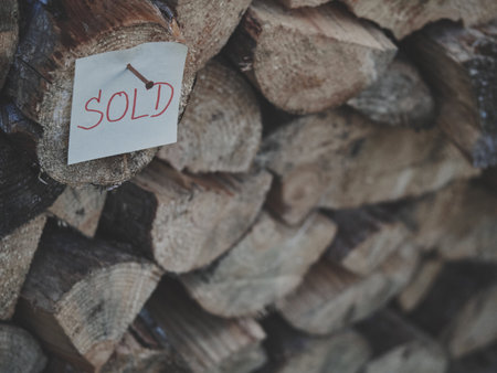 Close-up of firewood log with SOLD tag nailed on, background gradually blurred, warm matte tones, rustic texture, marketing concept, seasonal outdoor scene, natural cozy composition.の写真素材