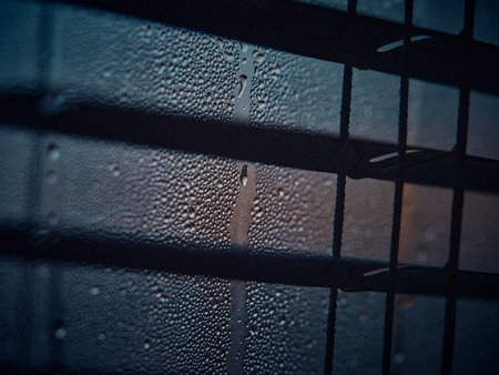Close view of window with dark blinds, condensation and raindrops in focus, soft morning light...